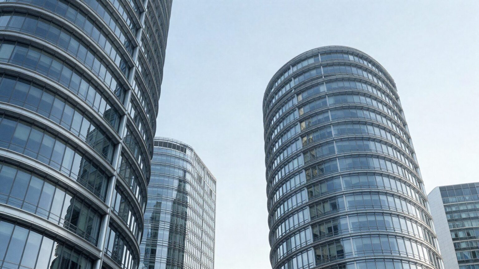 Curved glass office towers against a pale blue sky